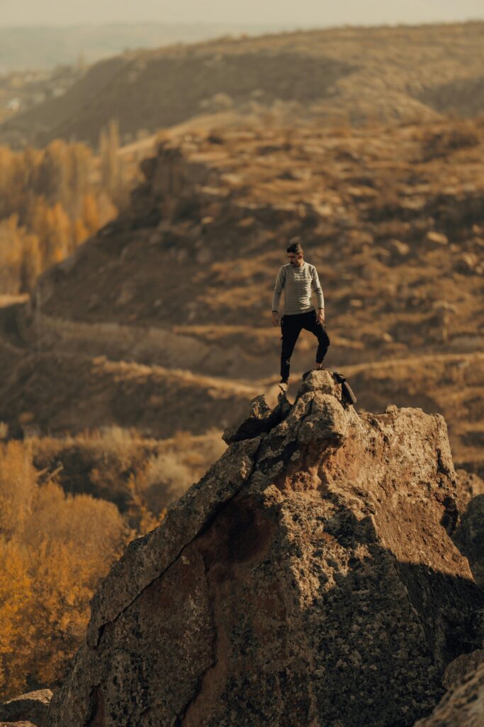 A lone hiker stands atop a rocky peak in İncesu, Kayseri, Türkiye, surrounded by autumn scenery.